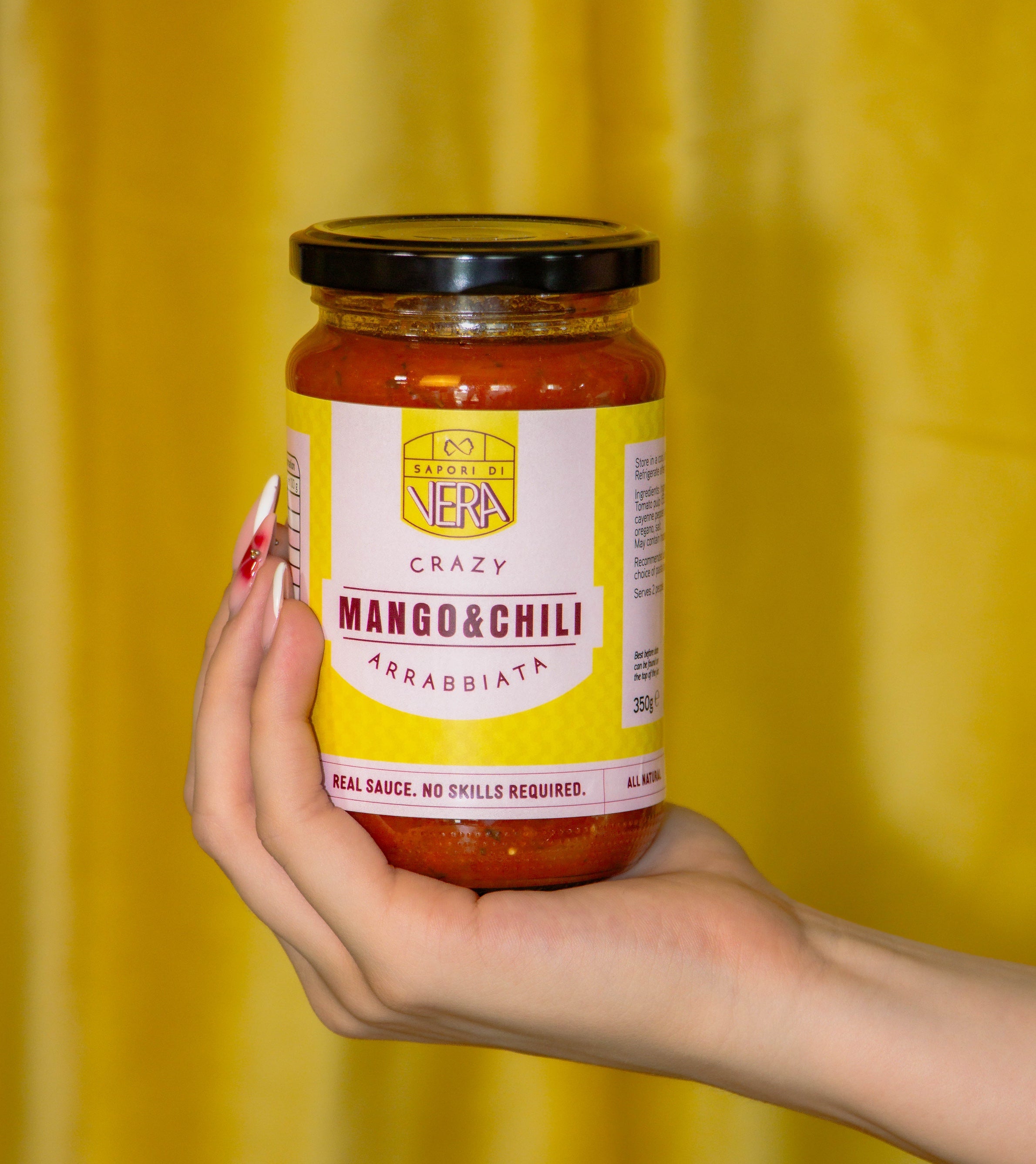 Hand holding a jar of 'Crazy Mango & Chili Arrabbiata' sauce against a yellow background