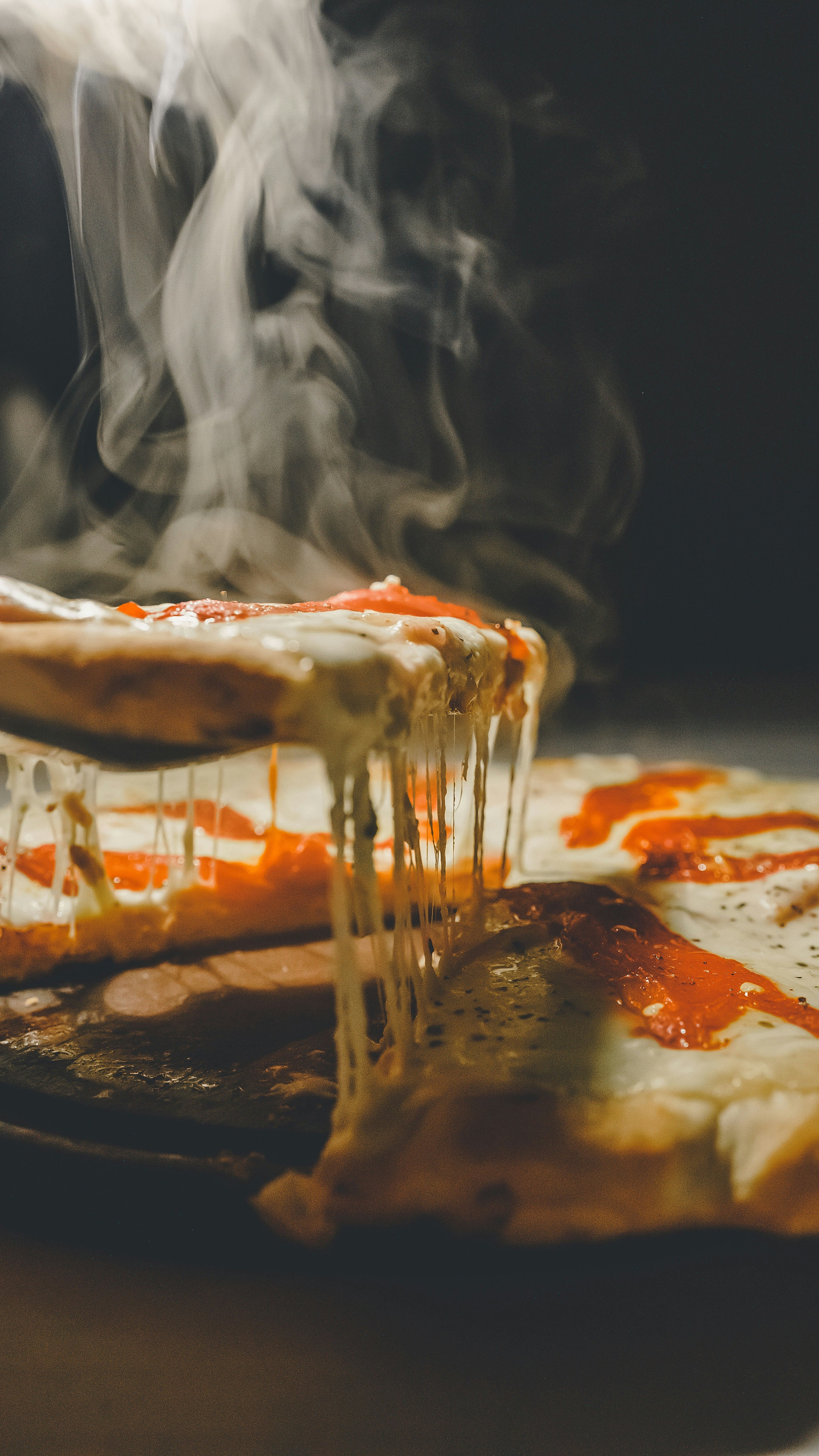 Steaming pizza with cheese stretching, dark background