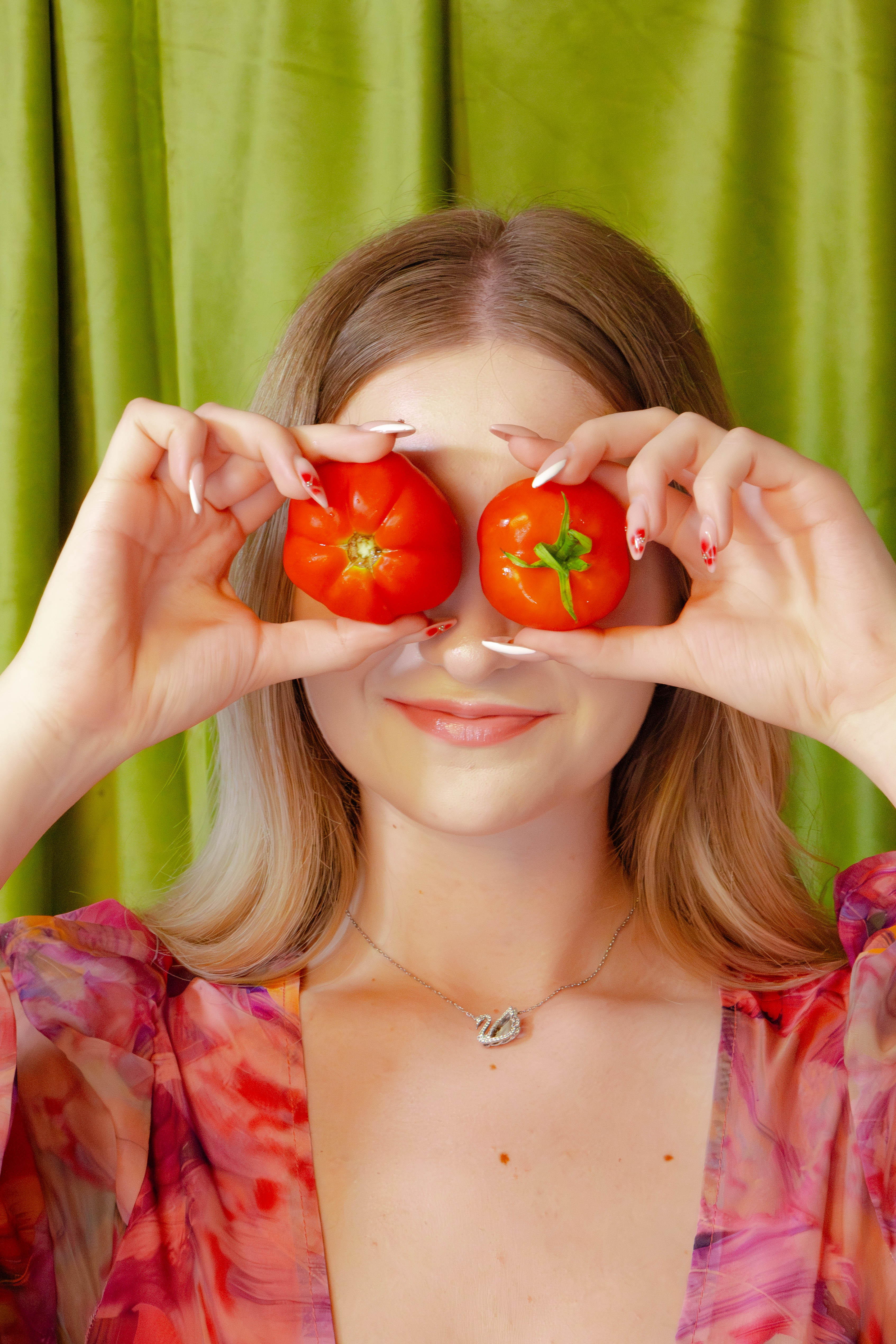 Woman holding two tomatoes in front of her eyes against a green curtain background
