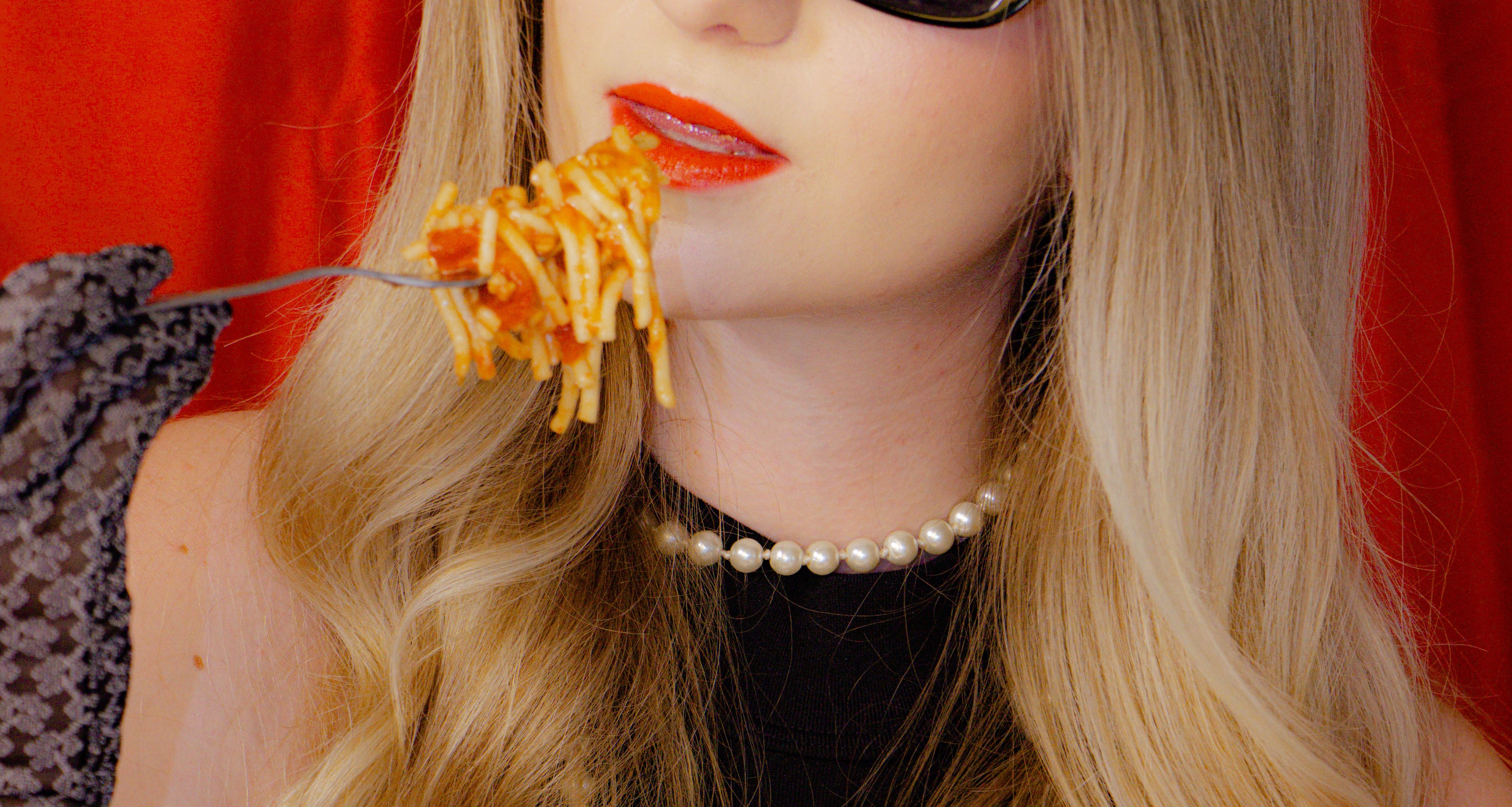 Person eating spaghetti with a fork against a red background