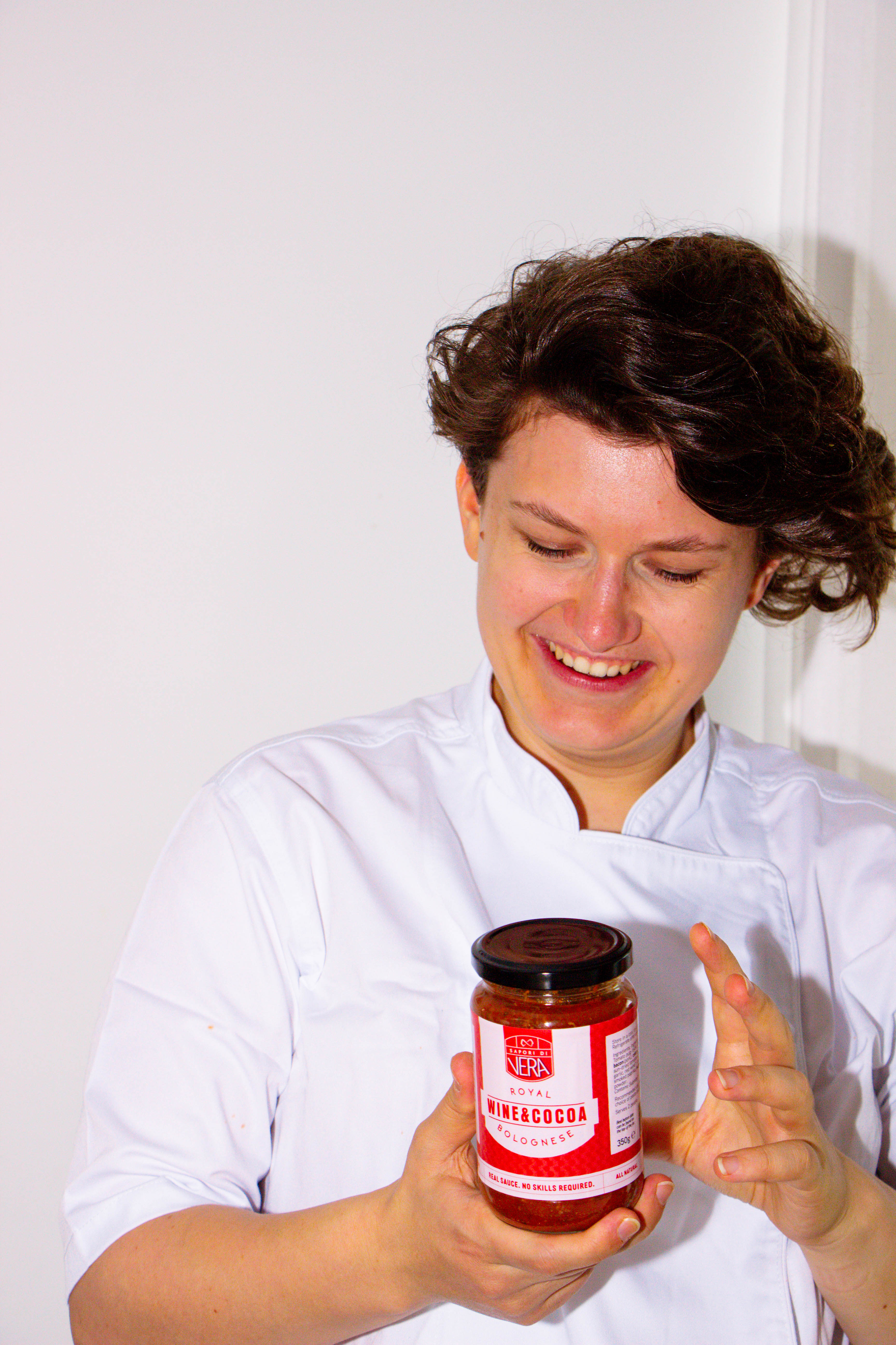 Person in a white coat holding a jar of pasta sauce against a white background
